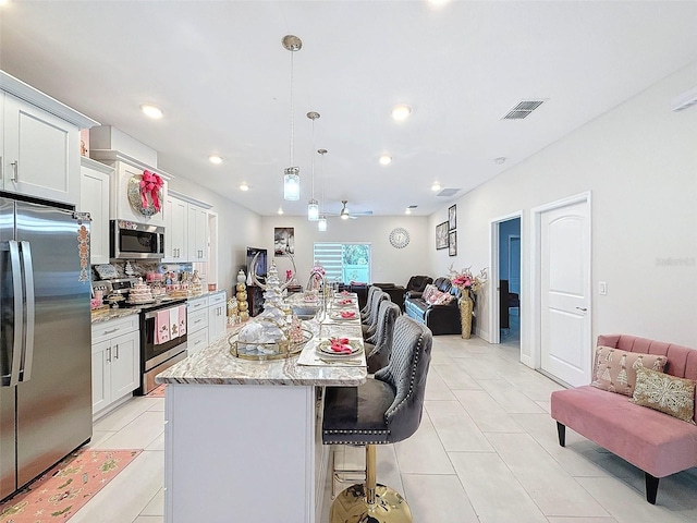 kitchen featuring a breakfast bar, stainless steel appliances, a kitchen island with sink, decorative light fixtures, and white cabinets