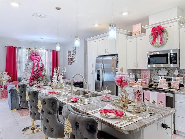 kitchen featuring pendant lighting, white cabinets, sink, an island with sink, and appliances with stainless steel finishes