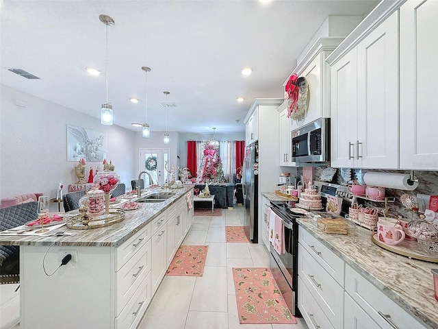 kitchen featuring appliances with stainless steel finishes, sink, white cabinets, hanging light fixtures, and an island with sink