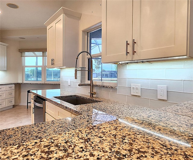 kitchen featuring light stone counters, backsplash, a sink, and white cabinets