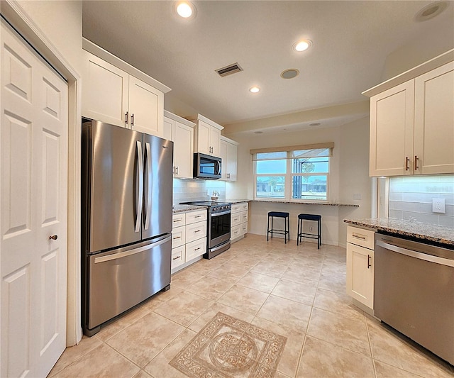 kitchen featuring stainless steel appliances, light stone counters, white cabinetry, and decorative backsplash