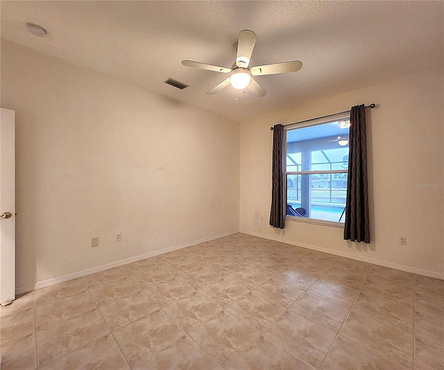 empty room with ceiling fan, a textured ceiling, visible vents, and baseboards