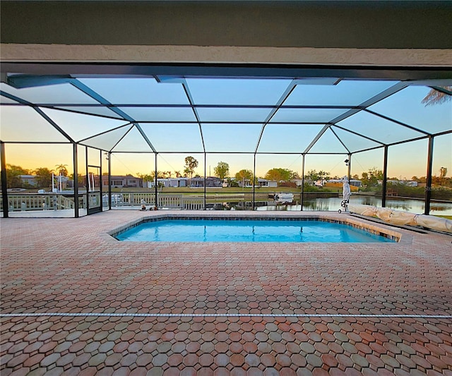 pool at dusk with glass enclosure, an outdoor pool, and a patio