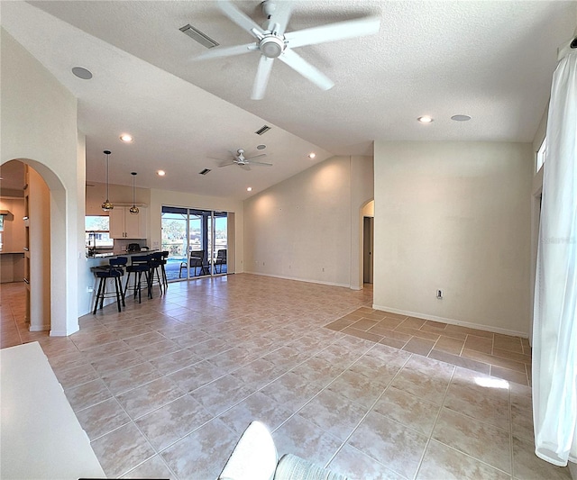 unfurnished living room featuring a ceiling fan, arched walkways, visible vents, and lofted ceiling