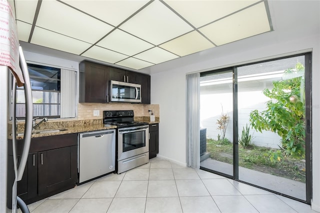 kitchen featuring decorative backsplash, appliances with stainless steel finishes, dark brown cabinetry, sink, and stone counters