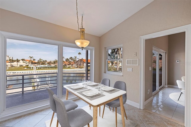 dining space featuring light tile patterned floors, a water view, vaulted ceiling, and a wealth of natural light