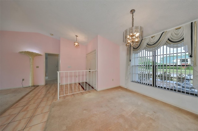 empty room featuring light colored carpet, lofted ceiling, a textured ceiling, and a chandelier