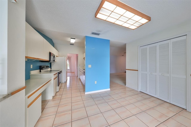 kitchen featuring white cabinetry, white appliances, a textured ceiling, and light tile patterned floors