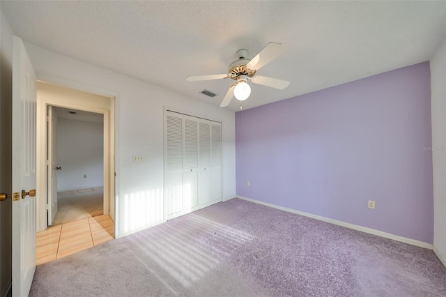 unfurnished bedroom featuring ceiling fan, a closet, light carpet, and a textured ceiling