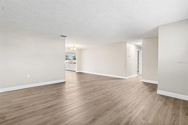 empty room featuring a textured ceiling, an inviting chandelier, and dark wood-type flooring