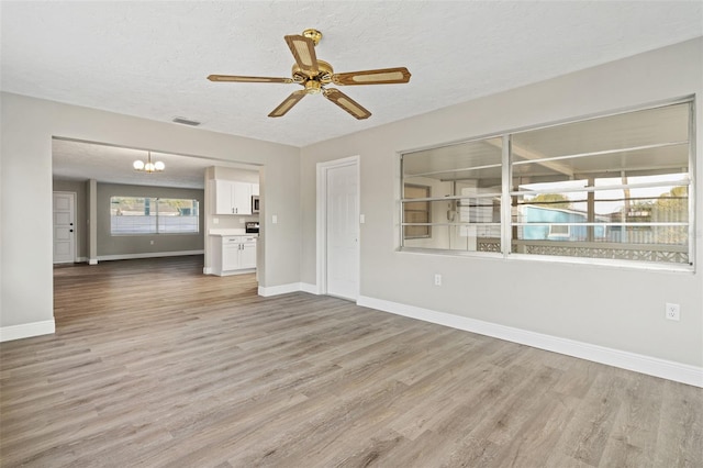 unfurnished living room with ceiling fan with notable chandelier, a textured ceiling, and light hardwood / wood-style flooring