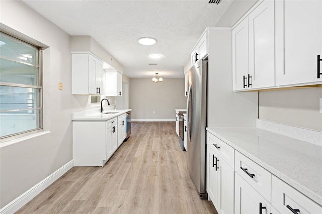 kitchen with appliances with stainless steel finishes, light stone counters, sink, light hardwood / wood-style flooring, and white cabinetry