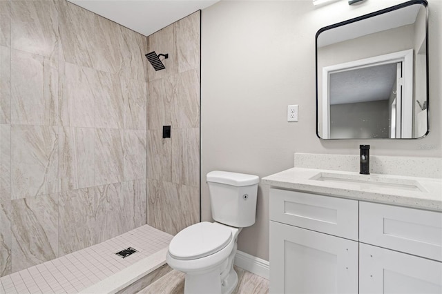 bathroom featuring a tile shower, vanity, wood-type flooring, and toilet