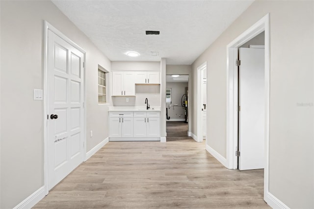 corridor with a textured ceiling, sink, and light hardwood / wood-style flooring