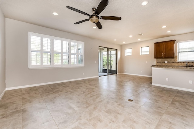 unfurnished living room featuring ceiling fan, sink, light tile patterned floors, and a textured ceiling