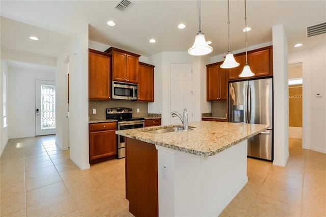 kitchen featuring sink, stainless steel appliances, light stone counters, decorative light fixtures, and a kitchen island with sink