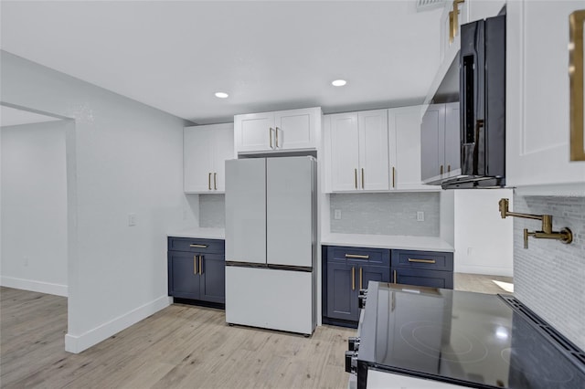 kitchen with blue cabinetry, white cabinetry, backsplash, light hardwood / wood-style floors, and white fridge