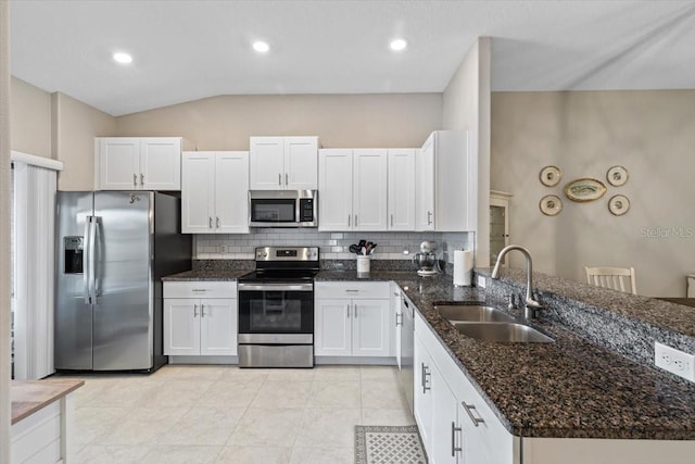 kitchen with lofted ceiling, dark stone counters, sink, appliances with stainless steel finishes, and white cabinetry