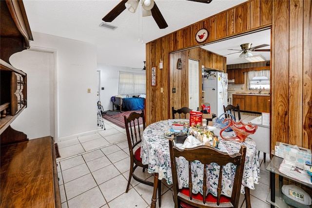 tiled dining space with sink, a textured ceiling, ceiling fan, and wood walls