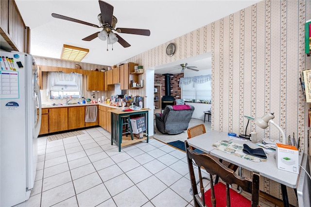 kitchen featuring ceiling fan, sink, white fridge, a wood stove, and light tile patterned flooring