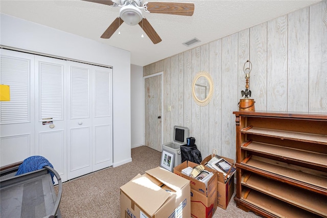 interior space featuring ceiling fan, light colored carpet, a textured ceiling, and wooden walls