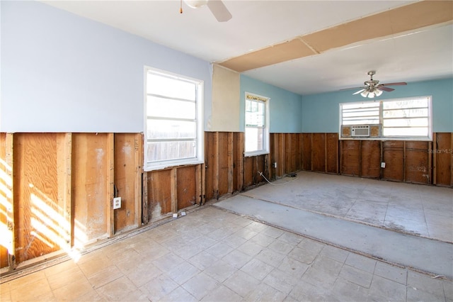 unfurnished room with cooling unit, wooden walls, ceiling fan, and a healthy amount of sunlight