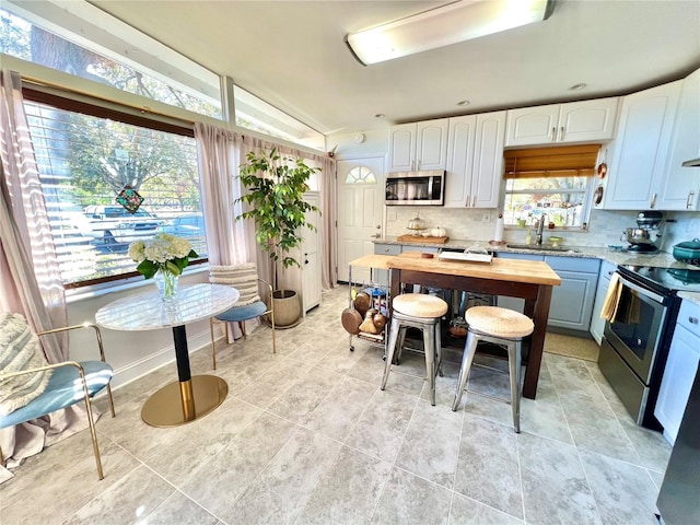 kitchen featuring sink, stainless steel appliances, tasteful backsplash, lofted ceiling, and white cabinets