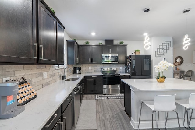 kitchen with sink, hanging light fixtures, tasteful backsplash, light hardwood / wood-style floors, and appliances with stainless steel finishes