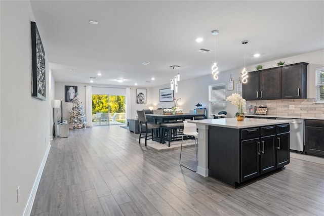 kitchen featuring pendant lighting, dishwasher, decorative backsplash, light wood-type flooring, and a kitchen island