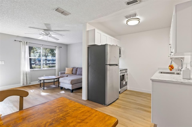 kitchen featuring appliances with stainless steel finishes, light wood-type flooring, ceiling fan, sink, and white cabinets