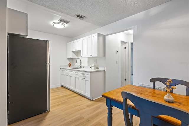 kitchen with stainless steel refrigerator, white cabinetry, sink, light hardwood / wood-style flooring, and a textured ceiling