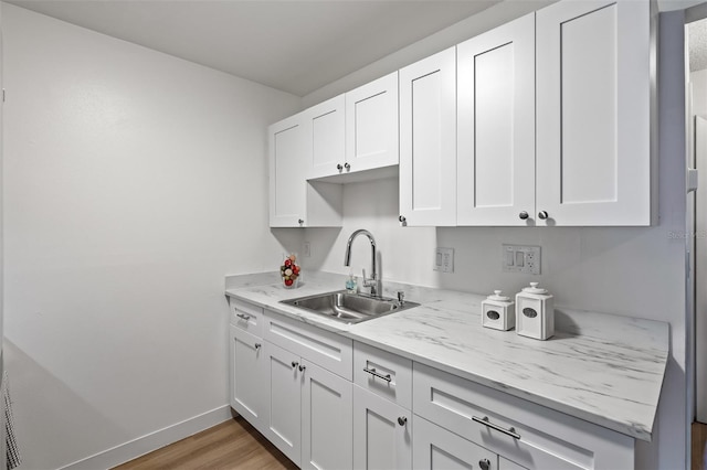 kitchen with white cabinetry, sink, light stone counters, and hardwood / wood-style flooring