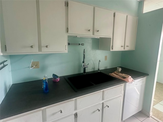 kitchen featuring white cabinets, dishwasher, dark countertops, a sink, and light tile patterned flooring