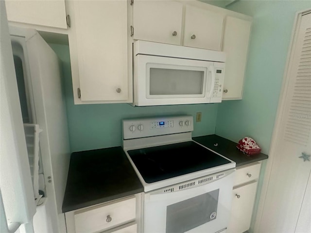 kitchen with dark countertops, white appliances, and white cabinetry