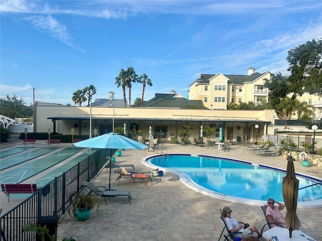 view of swimming pool featuring shuffleboard, a patio, and fence