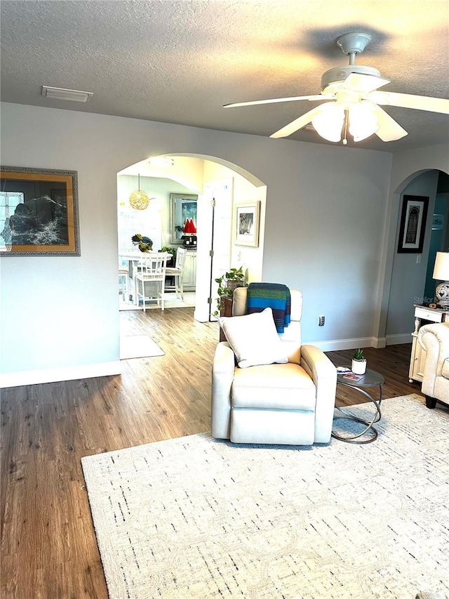 living room with a textured ceiling, ceiling fan, and wood-type flooring