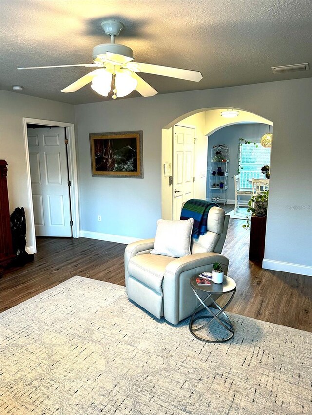 living room featuring ceiling fan, a textured ceiling, and dark hardwood / wood-style flooring