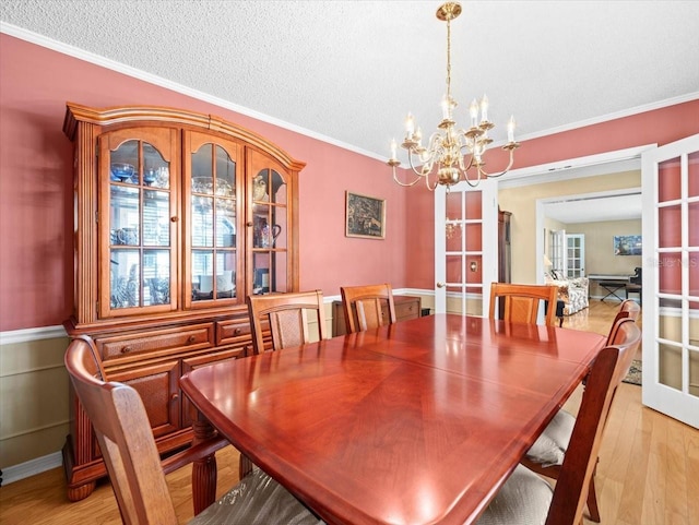 dining area featuring french doors, light wood-type flooring, a textured ceiling, and crown molding