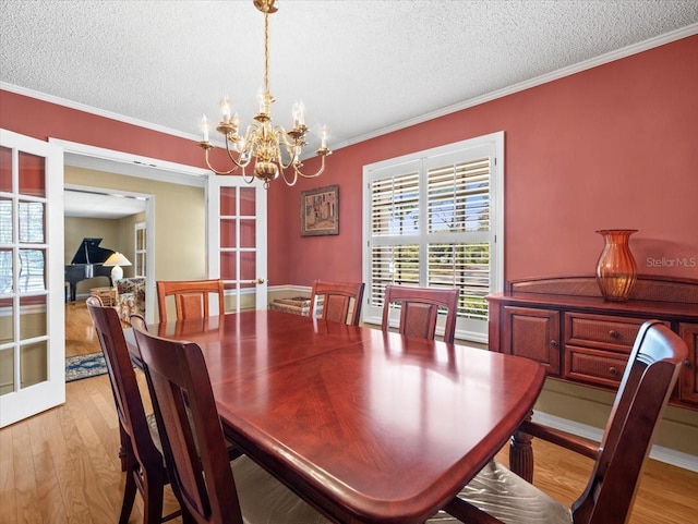 dining space featuring a textured ceiling, light hardwood / wood-style floors, an inviting chandelier, and ornamental molding