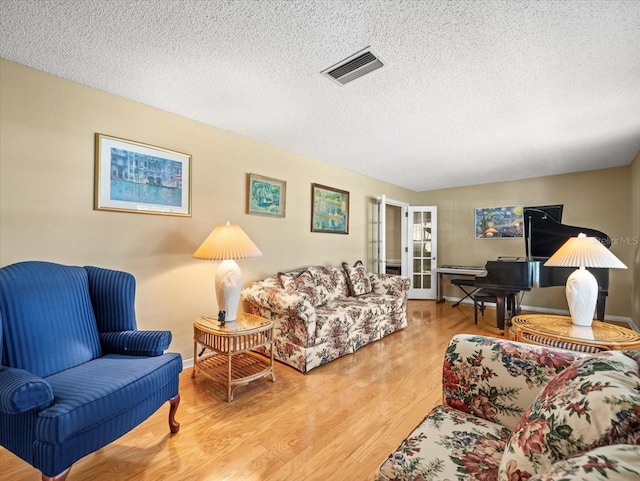 living room featuring french doors, light hardwood / wood-style floors, and a textured ceiling