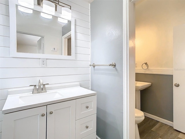 half bathroom with toilet, wood finished floors, and vanity