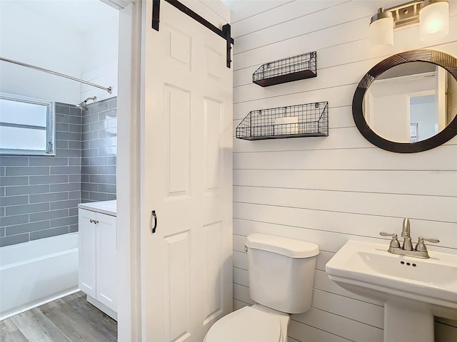 bathroom featuring toilet, tub / shower combination, a sink, wooden walls, and wood finished floors