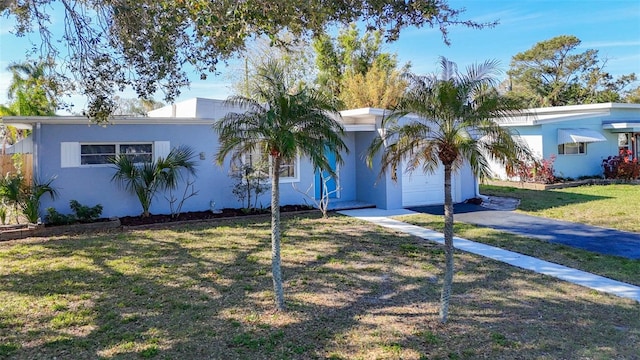 single story home with a garage, driveway, a front yard, and stucco siding