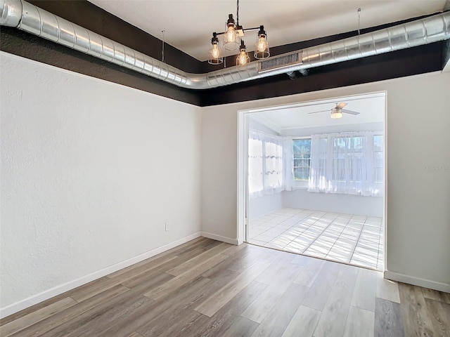 empty room featuring ceiling fan with notable chandelier, wood finished floors, visible vents, and baseboards