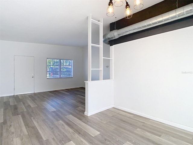 spare room with a notable chandelier, wood finished floors, and baseboards