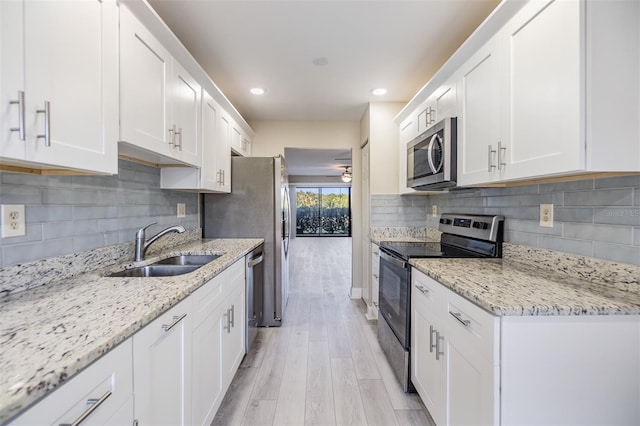 kitchen featuring sink, light stone countertops, light wood-type flooring, white cabinetry, and stainless steel appliances