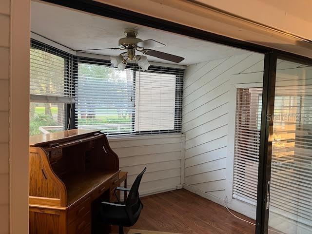 office area with wood walls, ceiling fan, and wood-type flooring