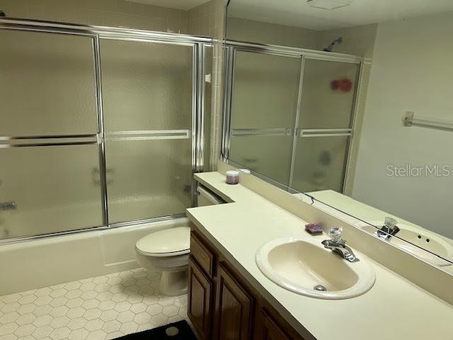 full bathroom featuring combined bath / shower with glass door, vanity, toilet, and tile patterned flooring