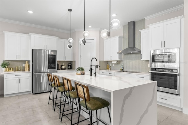 kitchen with white cabinetry, wall chimney range hood, a center island with sink, and appliances with stainless steel finishes