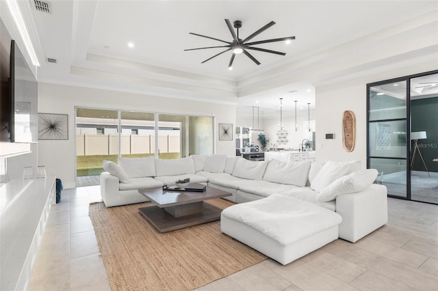 tiled living room with sink, crown molding, a raised ceiling, and ceiling fan